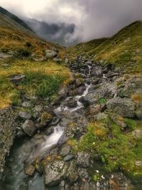 Stream flowing through rocks against sky