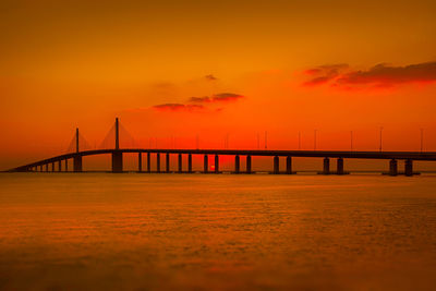 Bridge over calm sea against orange sky