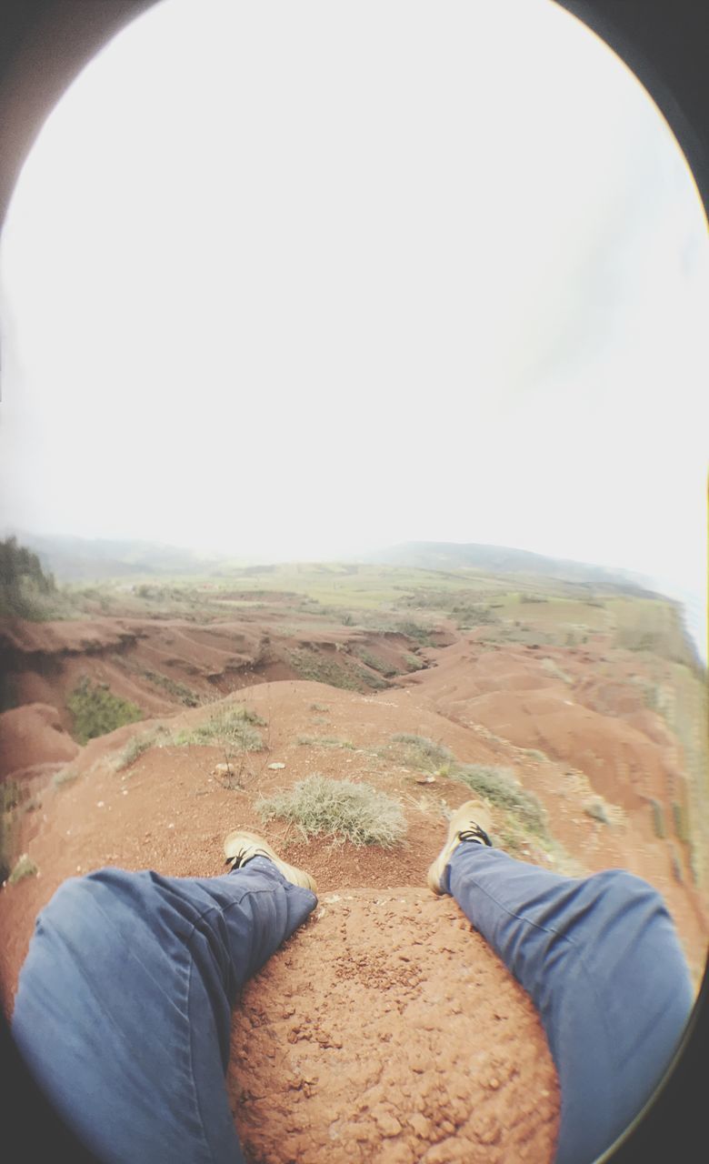 LOW SECTION OF MAN WEARING SHOES ON LANDSCAPE AGAINST SKY