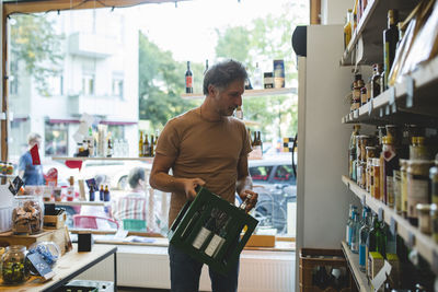 Mature salesman arranging bottle on shelf in deli