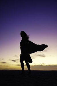 Silhouette woman with arms outstretched standing at sunset