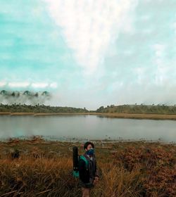 Man sitting by lake against sky