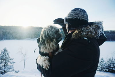 Side view of man with dog standing on snow covered field against sky