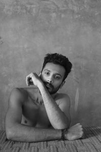 Portrait of young man sitting on floor against wall