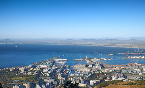 High angle view of townscape by sea against clear blue sky