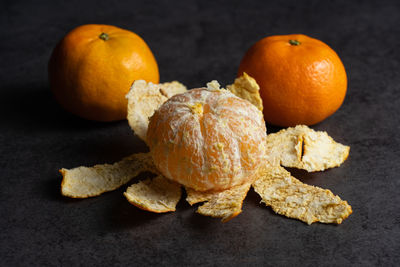 Three tangerines on a black background, one of them peeled