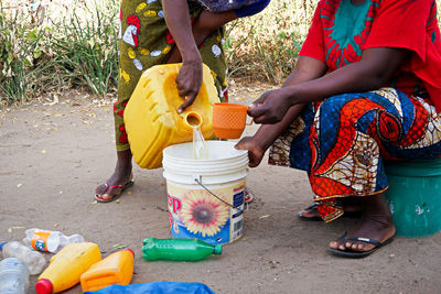 Low section of woman pouring water into bucket