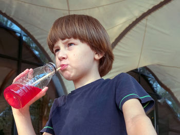 A boy in casual wear is drinking drinks soda from a bottle through a straw