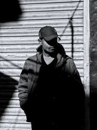 Young man standing against shutter during sunny day