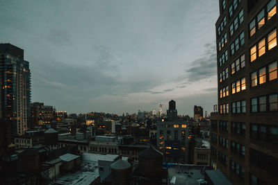 Illuminated buildings in city against sky at dusk