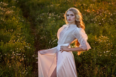 Beautiful young woman wearing white dress while standing on land at sunset