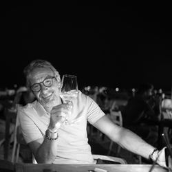 Portrait of happy man having wine in glass while sitting at outdoor restaurant during night