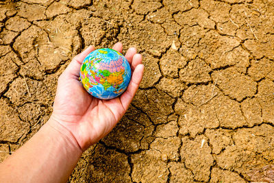 Cropped hand of person holding globe over dry field