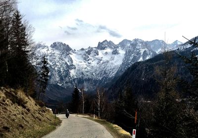 Road amidst trees and mountains against sky