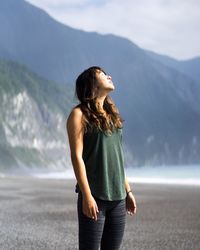 Young woman looking away while standing against mountain