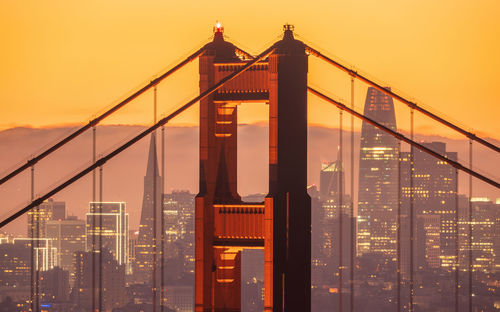 View of suspension bridge in city against sky during sunset