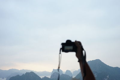Man photographing through smart phone against sky