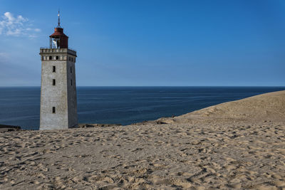 Lighthouse on beach against blue sky