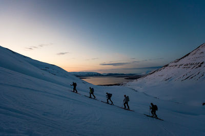 People on snow covered mountain against sky during sunset