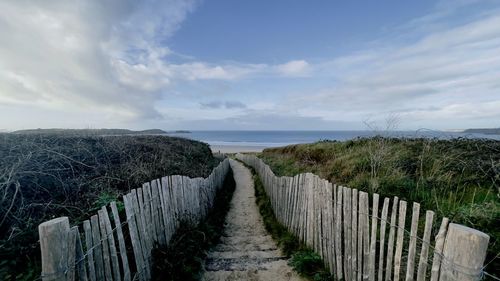 Footpath by fence on field against sky