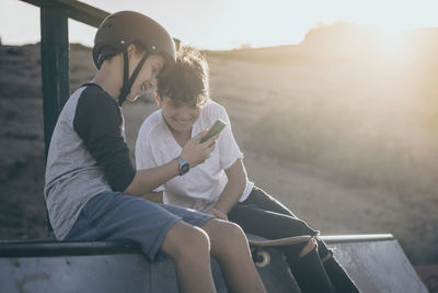 Friends looking at smart phone and smiling sitting outdoors