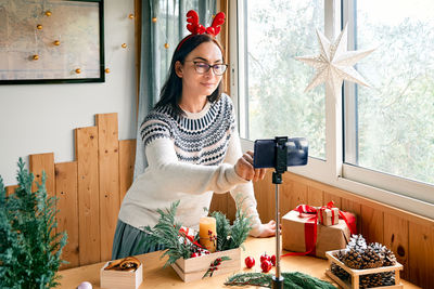 Female florist blogger making winter ikebana with pine branches, candle and christmas decorations