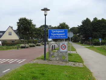 Road sign by trees against sky