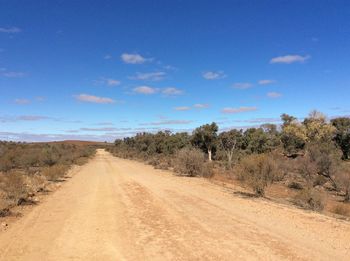 Dirt road passing through landscape against blue sky