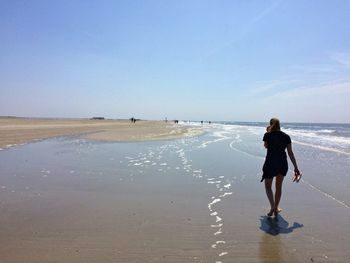 Rear view of woman walking on beach against sky