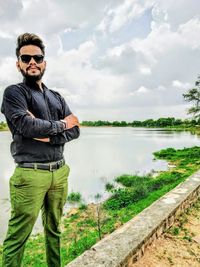 Portrait of young man standing by lake against sky