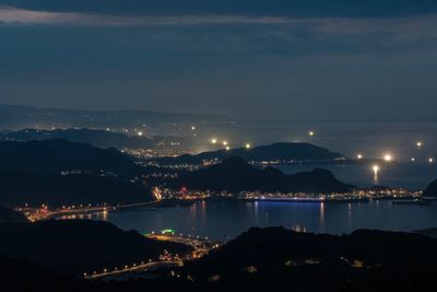 High angle view of illuminated city by sea against sky