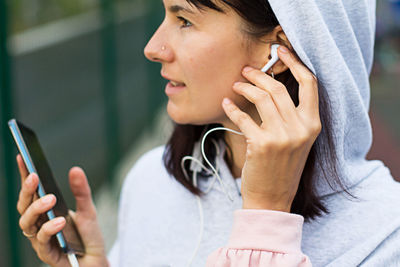 A caucasian woman uses a smartphone via wired headphones with a headset. phone in hand, white 