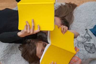 Young girl with her little brother enjoying reading together from yellow book.
