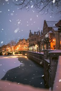 Illuminated buildings by canal in city during winter at night