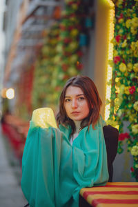 Portrait of beautiful woman holding illuminated jar and scarf while sitting in city at dusk