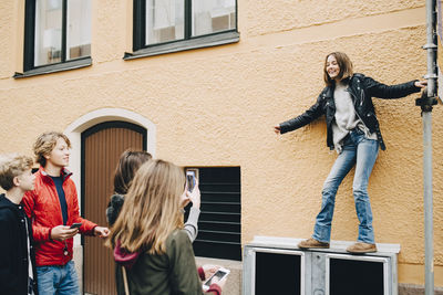 Female photographing girl while standing with friends at city