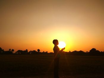 Silhouette man standing on field against sky during sunset