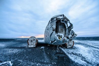 Abandoned boat on sea against sky during winter