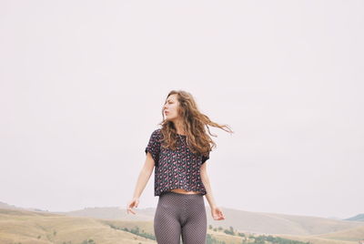 Young woman with tousled hair standing against clear sky