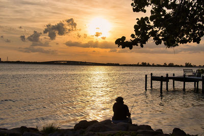 Silhouette people sitting on beach against sky during sunset