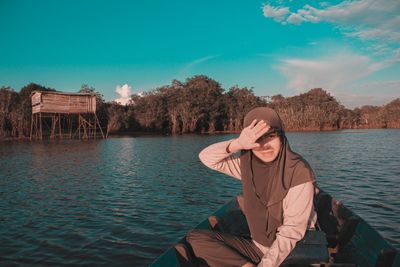 Woman sitting by lake against sky