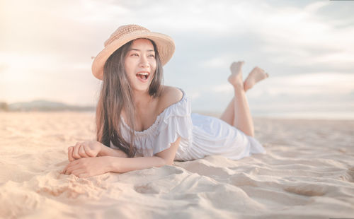 Young woman relaxing on sand at beach against sky