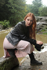 Portrait of young woman crouching on rock by river