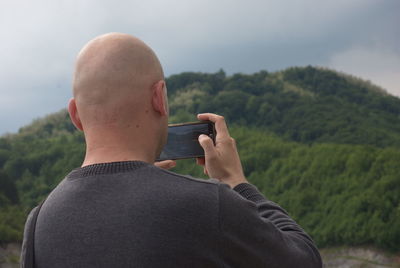 Rear view of bald man photographing mountain with mobile phone 
