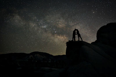 Low angle view of silhouette people on rock against sky at night