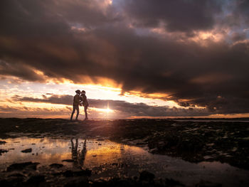 Couple kissing each other at beach against cloudy sky during sunset