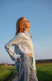 Side view of young woman standing against sky