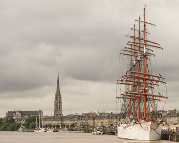 Sailboats in city against cloudy sky