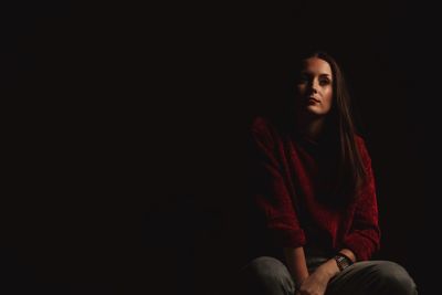 Young woman looking away while sitting against black background