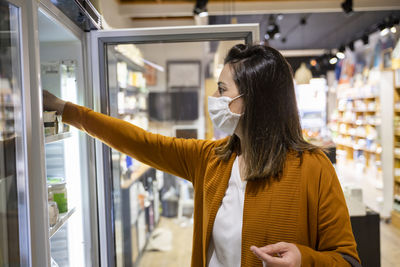 Young woman reaching for food in refrigerator at store